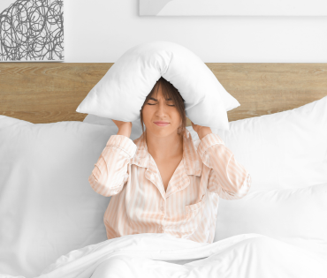 woman in bed with a white pillow over her head